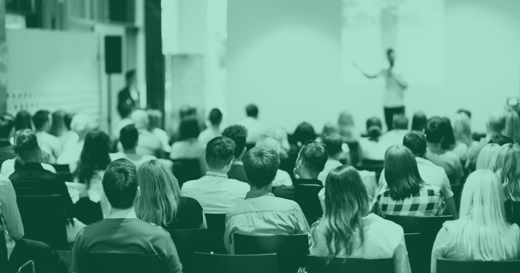 A series of attendants watch a speaker at an event